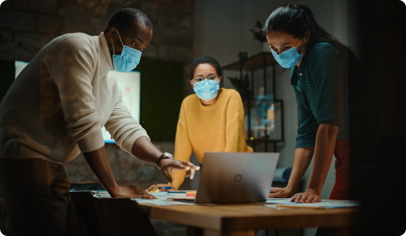 Three people wearing masks and looking at laptop