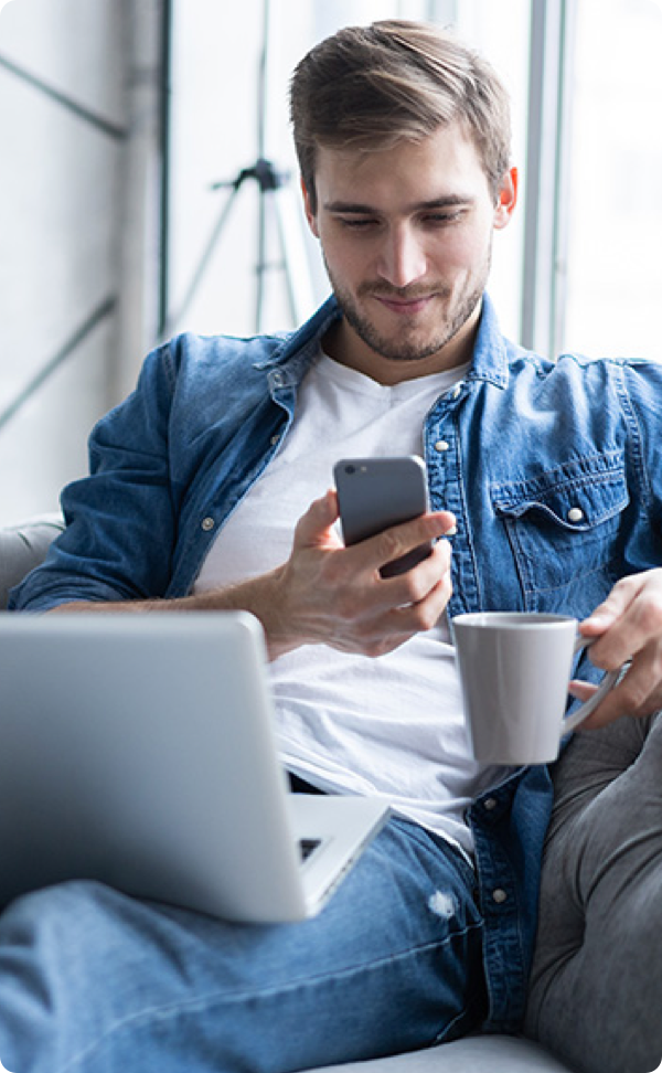 Man looking at phone with laptop on lap.