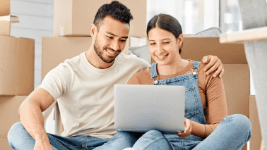 Couple sitting on ground smiling at laptop